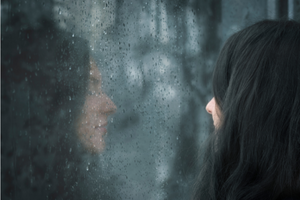woman stares at reflection in rainy window